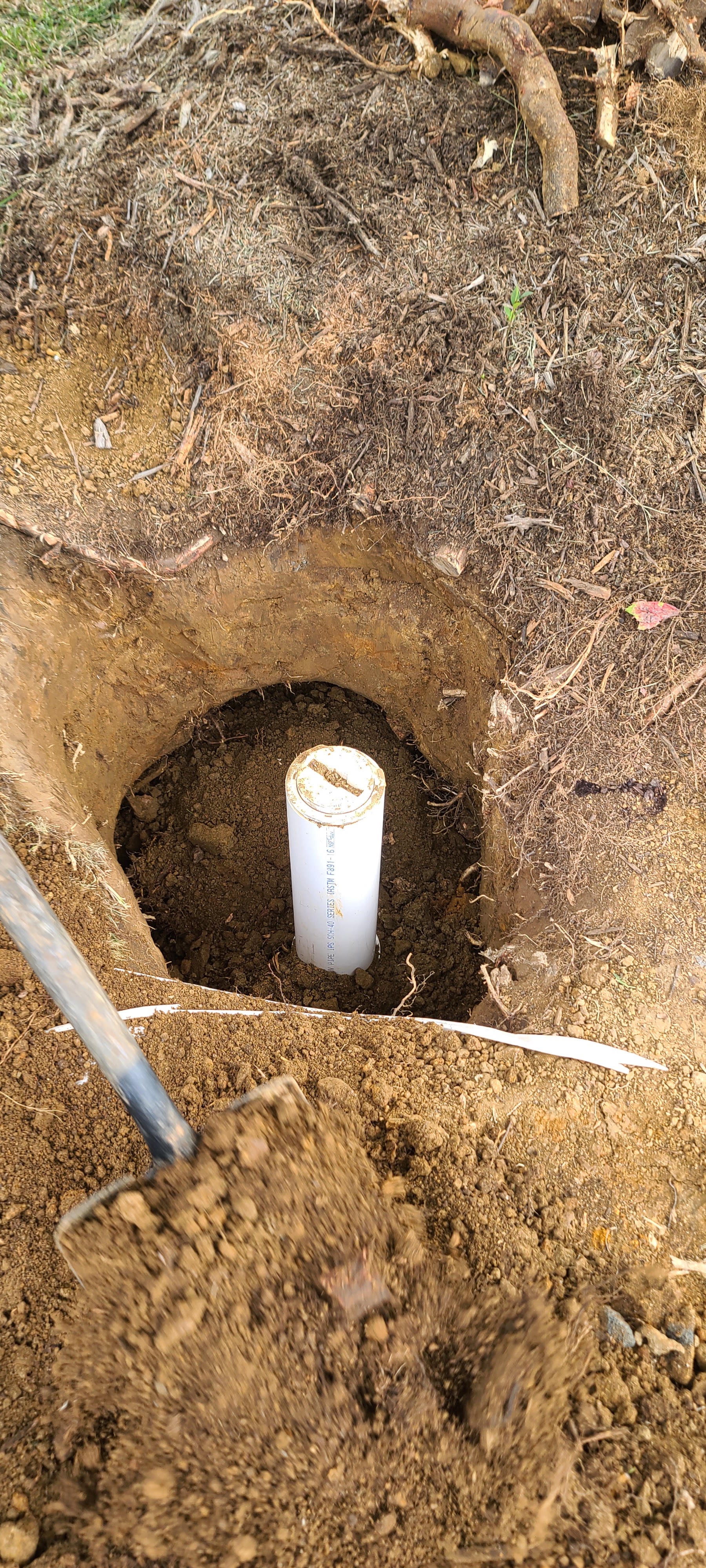White PVC pipe set in an excavated hole in the yard